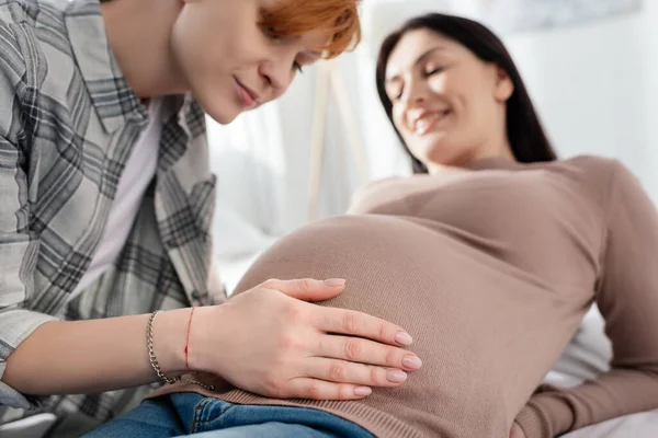 Concentration sélective de la femme touchant le ventre de la petite amie enceinte sur le lit — Photo de stock