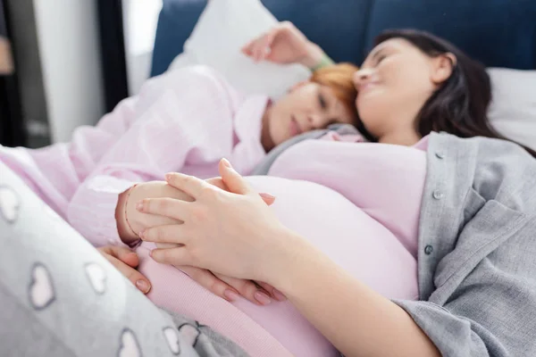 Focus selettivo della donna che tocca la pancia della fidanzata incinta mentre dorme sul letto — Foto stock
