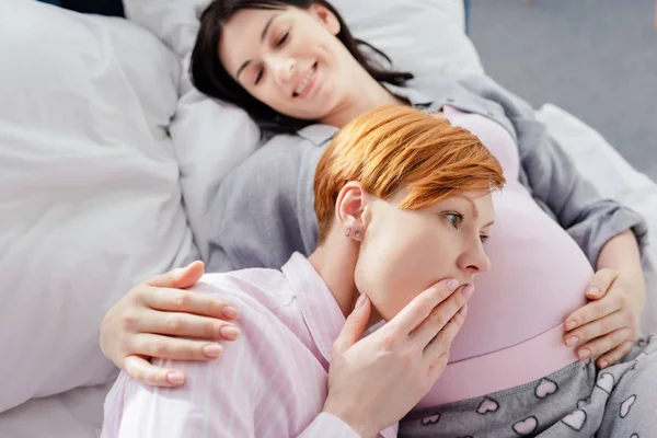 Mulher chocada ouvindo barriga de sorrir namorada grávida na cama — Fotografia de Stock