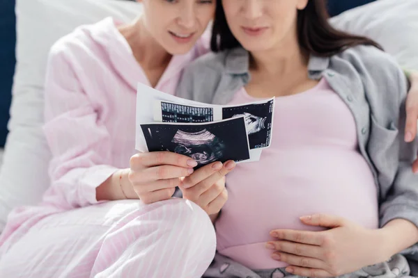 Selective focus of smiling same sex couple holding ultrasound scans of baby on bed isolated on blue — Stock Photo