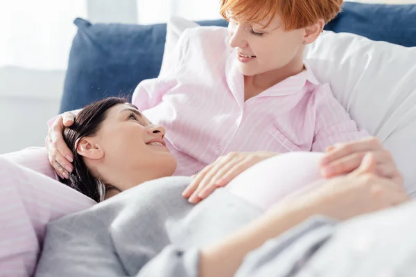 Enfoque selectivo de la mujer sonriendo a la novia embarazada en pijama en la cama en casa - foto de stock