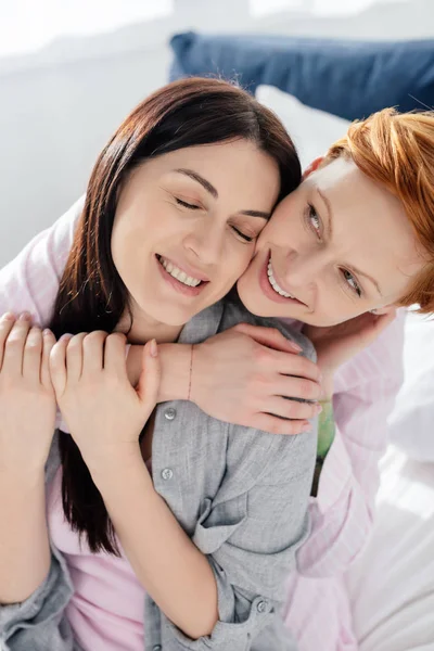 Smiling woman embracing cheerful girlfriend on bed — Stock Photo