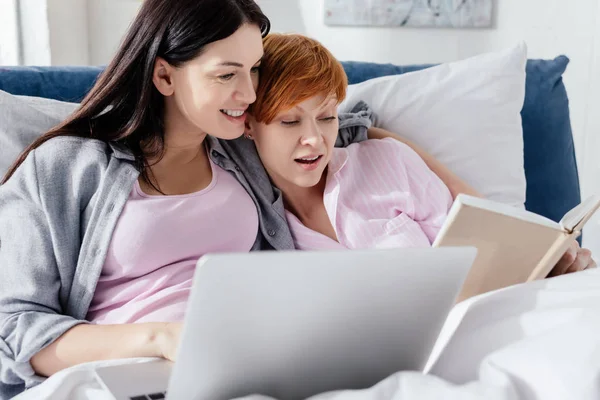 Gleichgeschlechtliches Paar liegt mit Laptop und Buch im Bett — Stockfoto