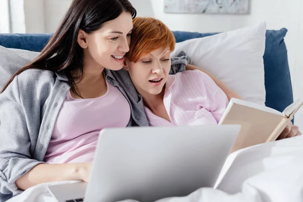 Same sex couple lying on bed with laptop and book — Stock Photo