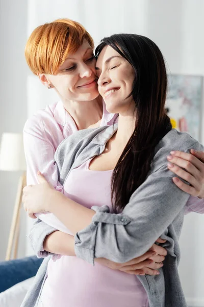 Sorrindo mulher abraçando namorada positiva no quarto — Fotografia de Stock