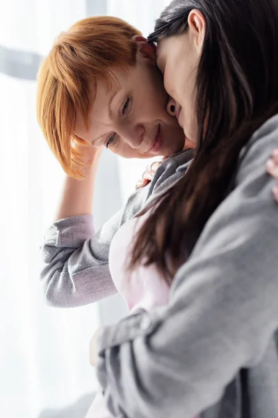 Side view of smiling woman embracing and looking at belly of pregnant girlfriend at home — Stock Photo