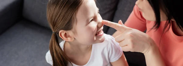 Panoramic shot of mother touching nose of smiling daughter at home — Stock Photo