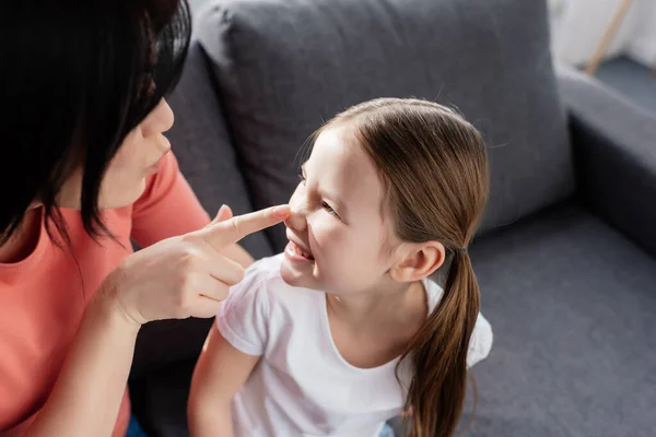 Mother touching nose of smiling daughter on couch at home — Stock Photo