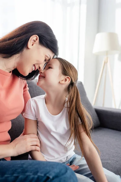 Lächelnde Mutter schaut glückliche Tochter zu Hause auf dem Sofa an — Stockfoto