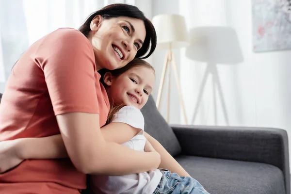 Sorrindo mulher abraçando feliz filha no sofá — Fotografia de Stock