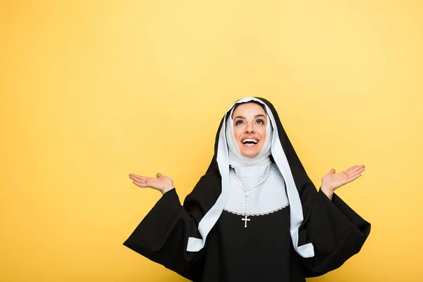 Cheerful nun praying and looking up, on yellow — Stock Photo