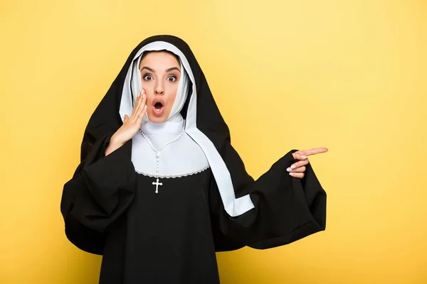 Belle nonne choquée pointant sur jaune — Photo de stock