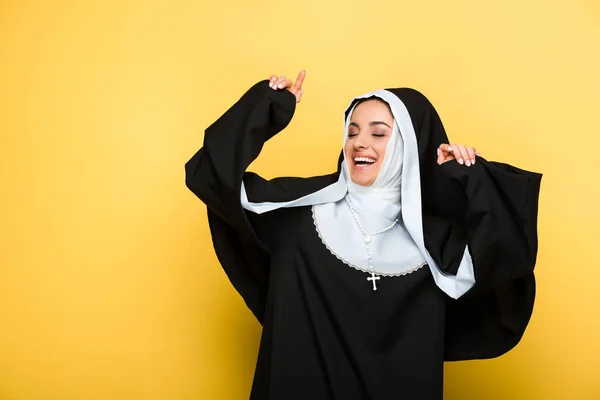 Beautiful cheerful nun dancing with closed eyes, on yellow — Stock Photo