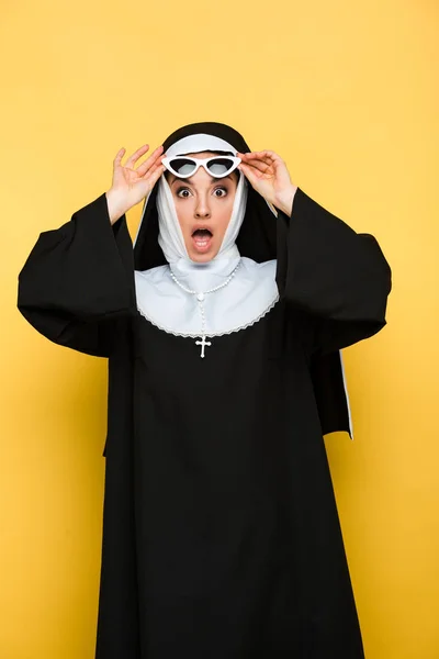 Atractiva monja sorprendida en gafas de sol aisladas en amarillo - foto de stock