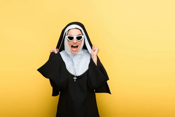 Attractive excited nun in sunglasses on yellow — Stock Photo