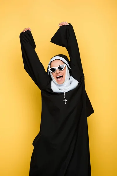 Attrayante nonne excitée dansant dans des lunettes de soleil isolées sur jaune — Photo de stock