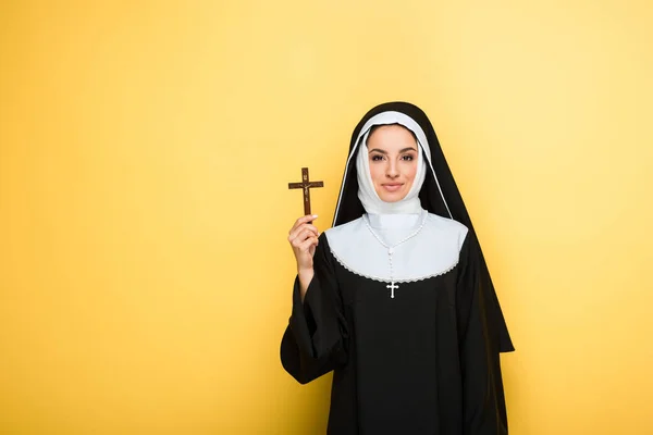 Красивая улыбающаяся монахиня держит крест изолирован на желтый — стоковое фото
