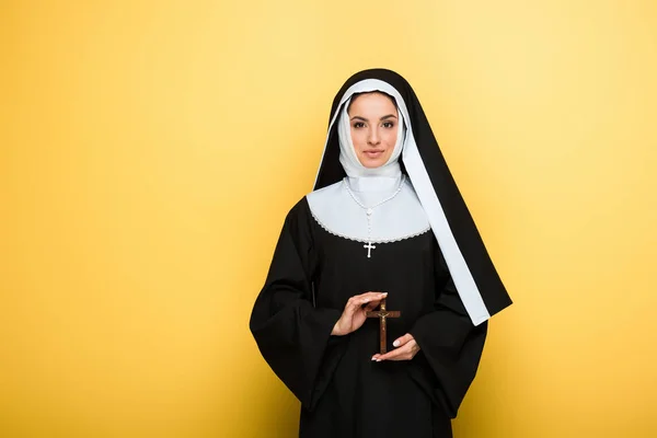 Schöne glückliche Nonne hält Kreuz auf gelb — Stockfoto