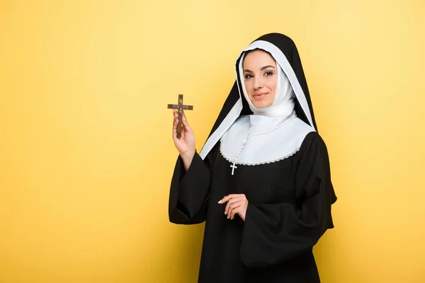 Attractive smiling nun holding cross on yellow — Stock Photo
