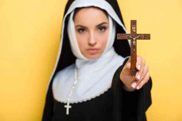 Selective focus of beautiful nun holding cross isolated on yellow — Stock Photo