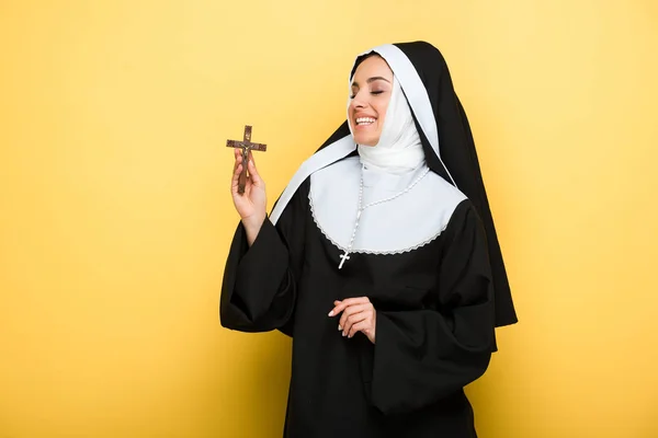 Bela freira alegre segurando cruz no amarelo — Fotografia de Stock