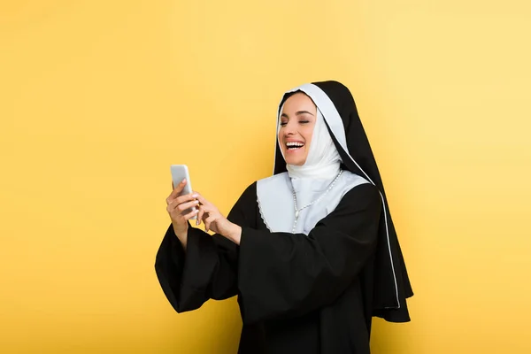 Hermosa monja emocionada usando teléfono inteligente en amarillo - foto de stock