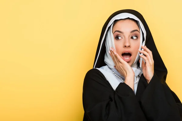 Belle nonne surprise parlant sur smartphone isolé sur jaune — Photo de stock