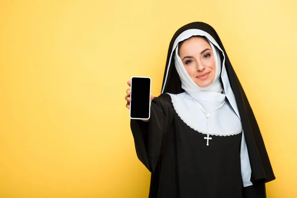 Hermosa monja mostrando teléfono inteligente con pantalla en blanco en amarillo - foto de stock