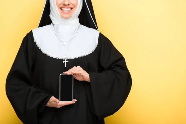 Обрезанный вид монахини, представляющей смартфон с пустым экраном на желтом — стоковое фото