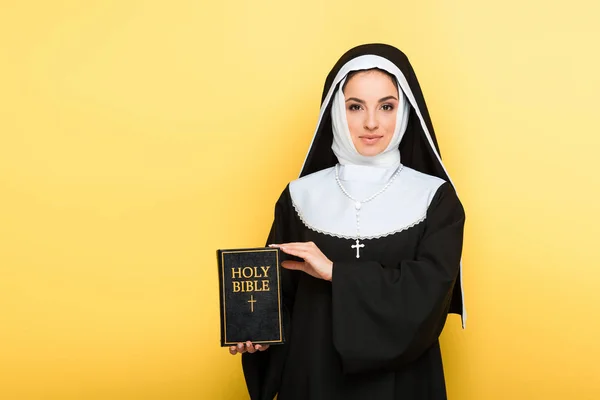 Beautiful smiling nun holding holy bible on grey — Stock Photo