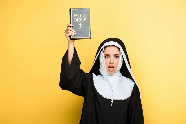 Shocked nun holding holy bible on grey — Stock Photo