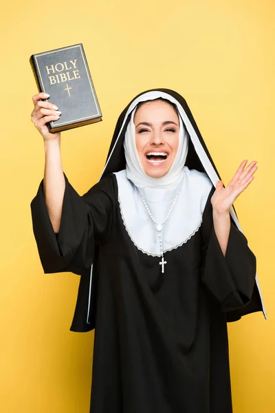 Hermosa monja excitada sosteniendo la sagrada biblia en gris - foto de stock