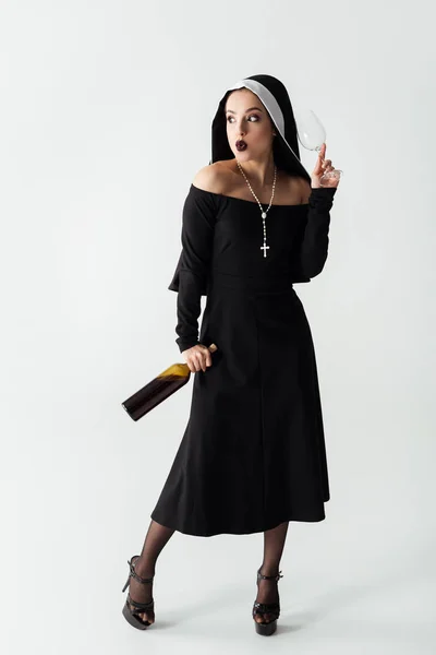 Attractive sexy nun holding glass and bottle of wine on grey — Stock Photo