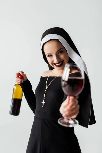 Selective focus of cheerful sexy nun holding glass and bottle of wine isolated on grey — Stock Photo