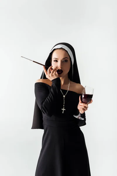 Beautiful sensual nun with glass of wine smoking a cigarette in mouthpiece isolated on grey — Stock Photo