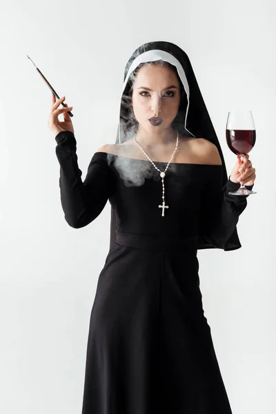 Passionate nun with glass of wine smoking a cigarette in mouthpiece isolated on grey — Stock Photo