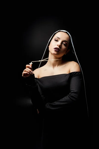 Sexy jovem freira no vestido preto segurando cruz, isolado no preto — Fotografia de Stock