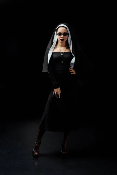 Belle nonne sexy en robe noire et lunettes de soleil, sur noir — Photo de stock