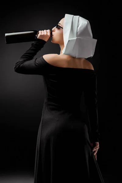 Attractive sexy nun in sunglasses drinking wine from bottle on grey — Stock Photo