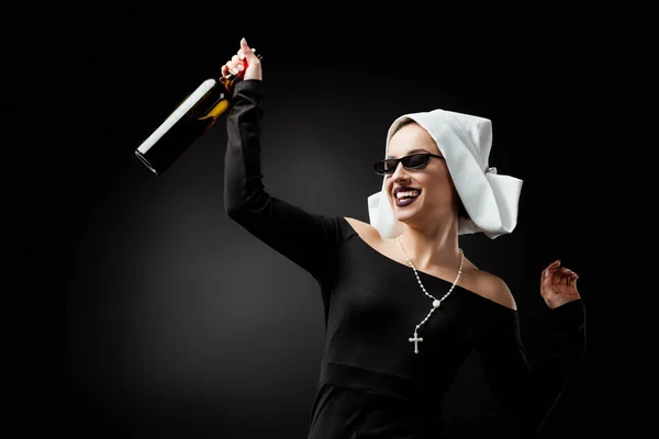 Jolie religieuse souriante dans des lunettes de soleil tenant bouteille de vin sur gris — Photo de stock