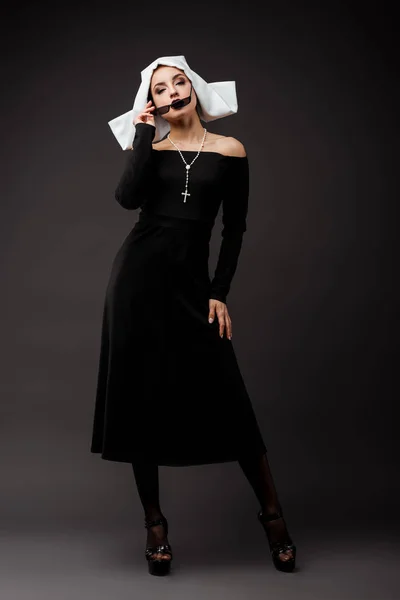 Sexy nun in black dress and sunglasses, on grey — Stock Photo