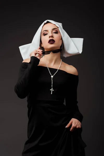 Привлекательная сексуальная монахиня в черном платье и солнцезащитных очках, изолированная на сером — стоковое фото