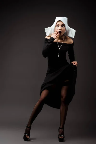 Monja sexy impactada en vestido negro y medias, en gris - foto de stock