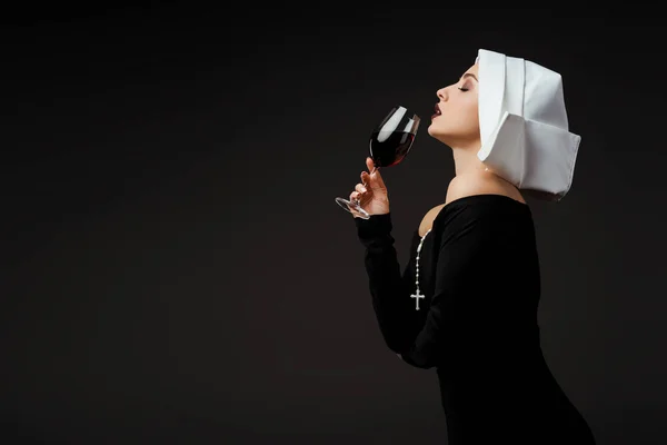 Attractive passionate nun drinking red wine from glass isolated on grey — Stock Photo