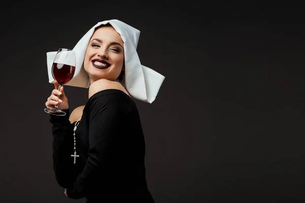 Cheerful sexy nun holding glass of red wine isolated on grey — Stock Photo