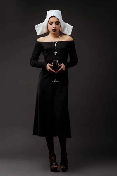 Attraktive nachdenkliche Nonne mit einem Glas Rotwein auf grau — Stockfoto