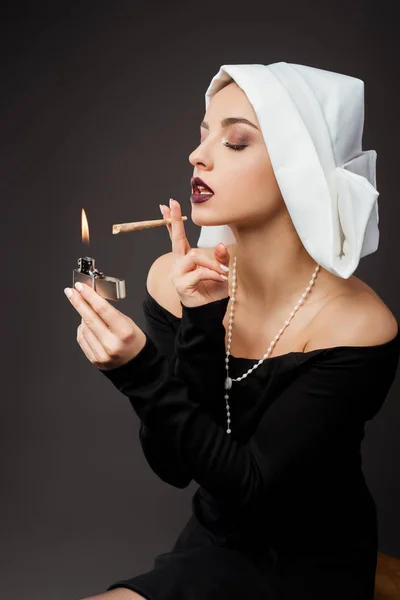 Attractive sexy nun smoking marijuana joint with lighter on grey — Stock Photo