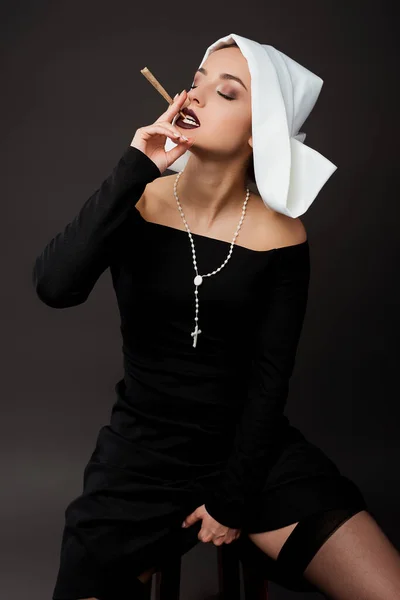 Attractive sexy nun smoking marijuana joint on grey — Stock Photo