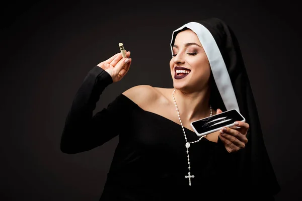 Happy nun holding dollar banknote and smartphone with cocaine lines isolated on grey — Stock Photo