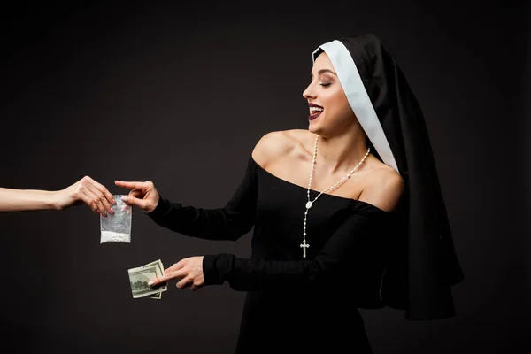 Smiling sexy nun with money buying plastic bag of cocaine isolated on grey — Stock Photo